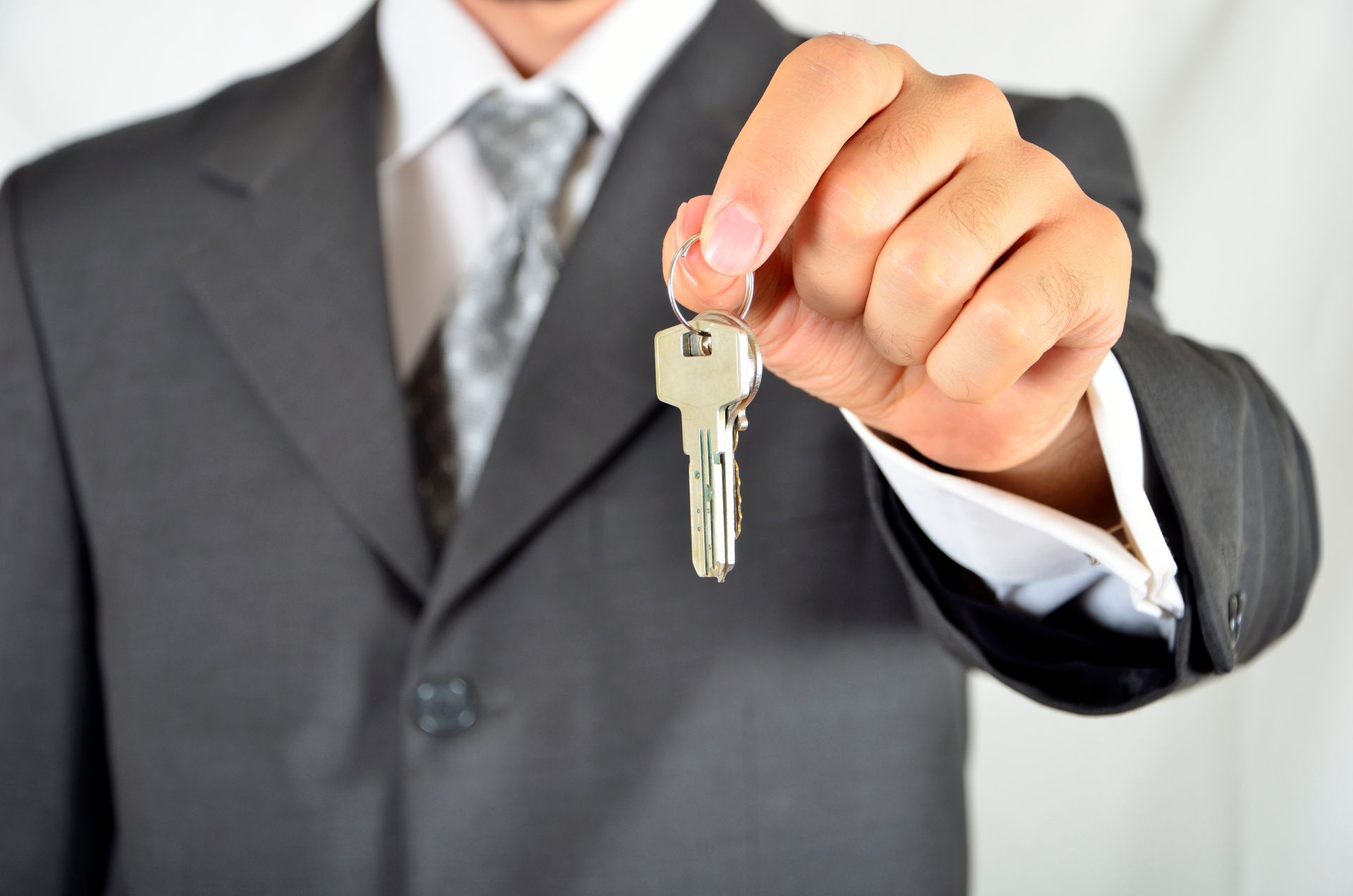 Man in suit holding keys, focus on hand in foreground, showcasing importance of commercial re-keys.