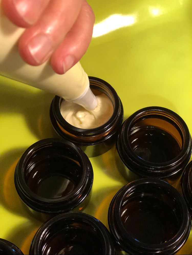 A person is pouring NOM NATURALS into a small jar