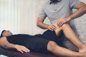 A man is laying on a table getting his knee examined by a doctor.