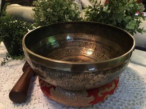 A singing bowl is sitting on a table next to a plant.