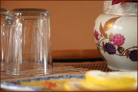 A vase with flowers on it sits on a table next to empty glasses