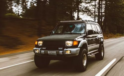A black suv is driving down a road in the woods.