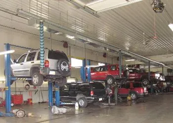 Cars on lifts inside an auto repair shop; several vehicles are undergoing service.