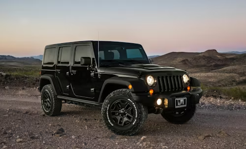 Black Jeep Wrangler parked on a rocky trail at dusk under a pink sky