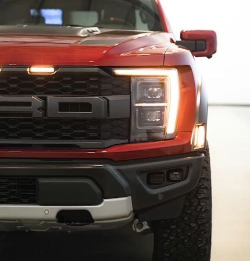 Front view of a red Ford truck with headlights on, shown indoors
