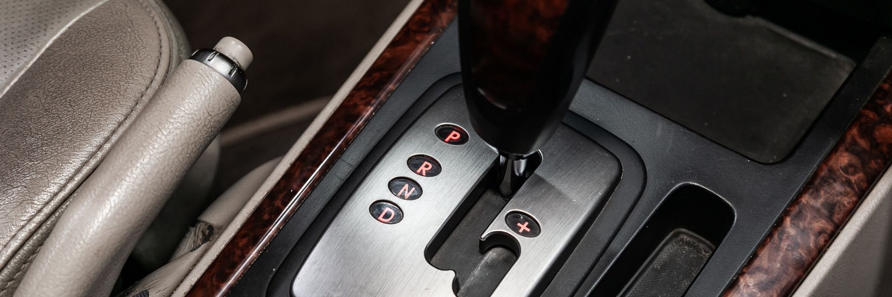 Interior car shot showing an automatic gear shift lever in a silver console, with a wood-grain trim. A handbrake is visible on the left.