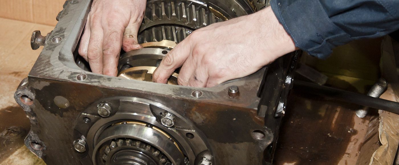Hands working on a complex gear mechanism, possibly repairing or assembling it.