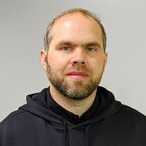 A man with a beard is wearing a black hoodie and looking at the camera.