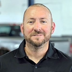 A man with a beard is wearing a black shirt and smiling for the camera.