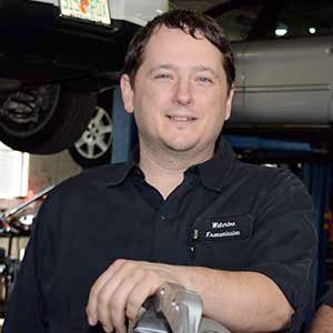 A man in a black shirt is standing in front of a car.