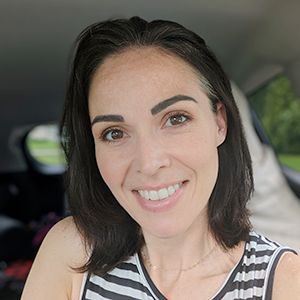 A woman is smiling while sitting in the back seat of a car.