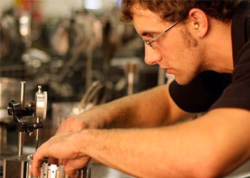 A man wearing glasses is working on a machine in a factory.