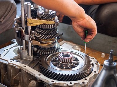 A person is working on a gearbox with a screwdriver.