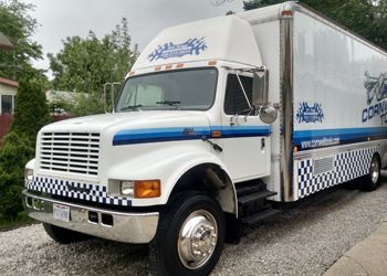 A white truck with a blue and white checkered stripe on the side is parked on gravel.