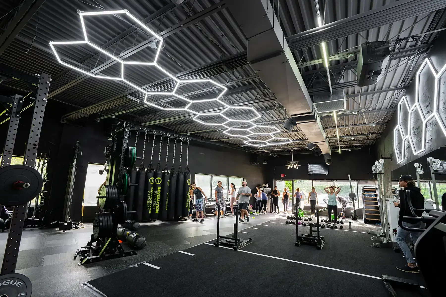 Revolution Fitness in East Northport, NY. Modern gym interior with hexagonal ceiling lights, workout equipment, and people exercising