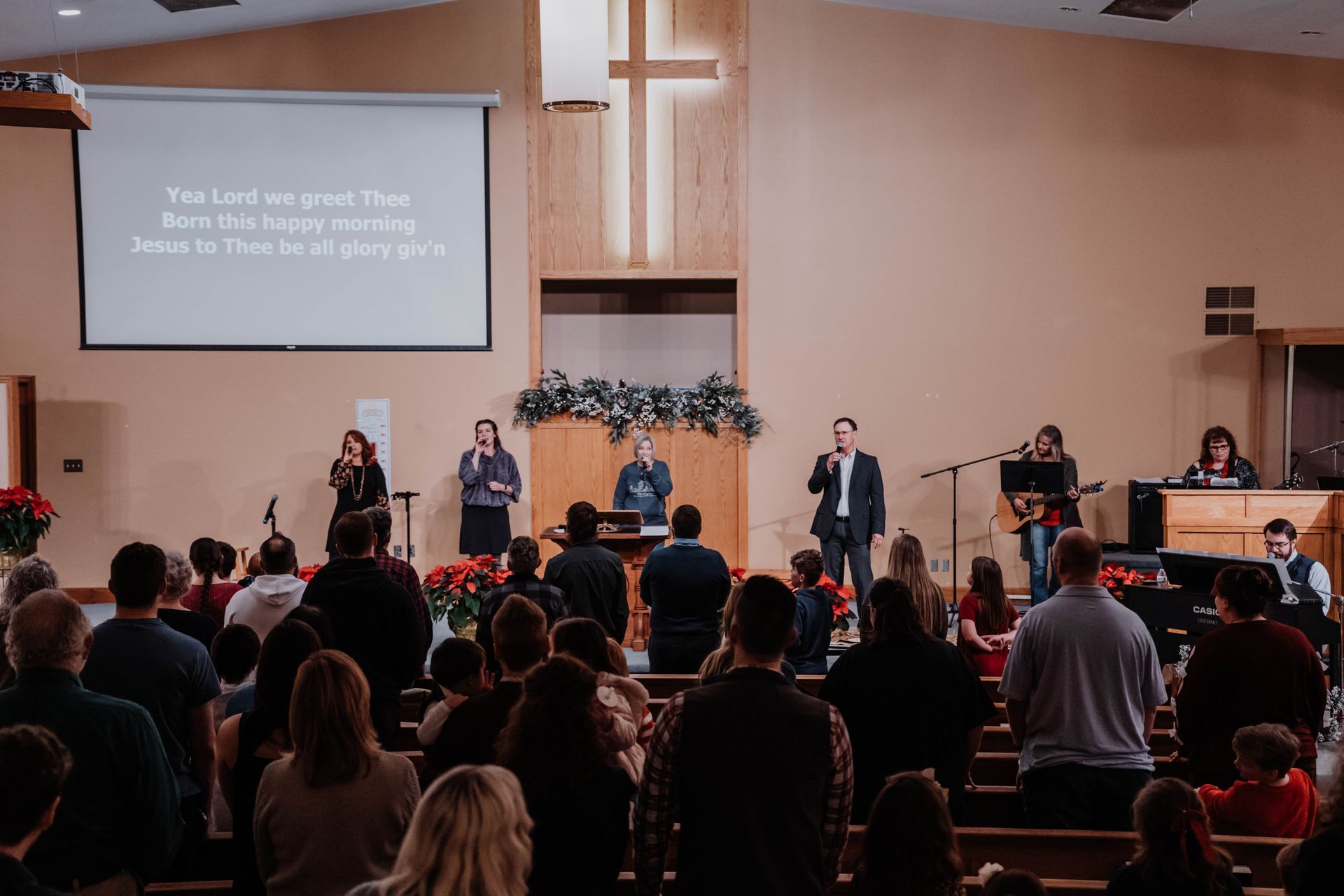 People worshiping in a church with a cross, stage, and band performing.