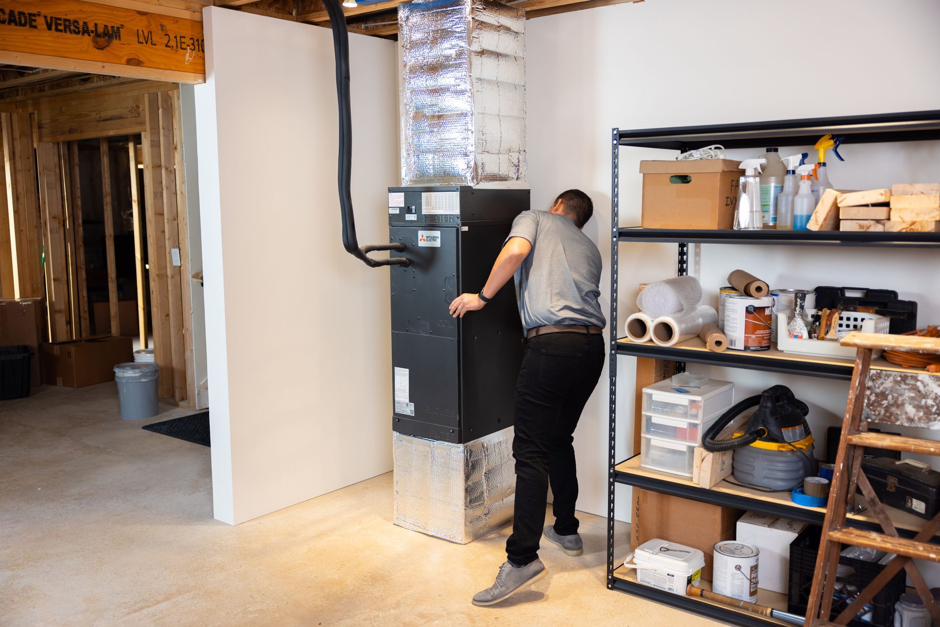 Pfluke Home Services technician inspecting a furnace in a basement. The furnace is black, next to a shelf.