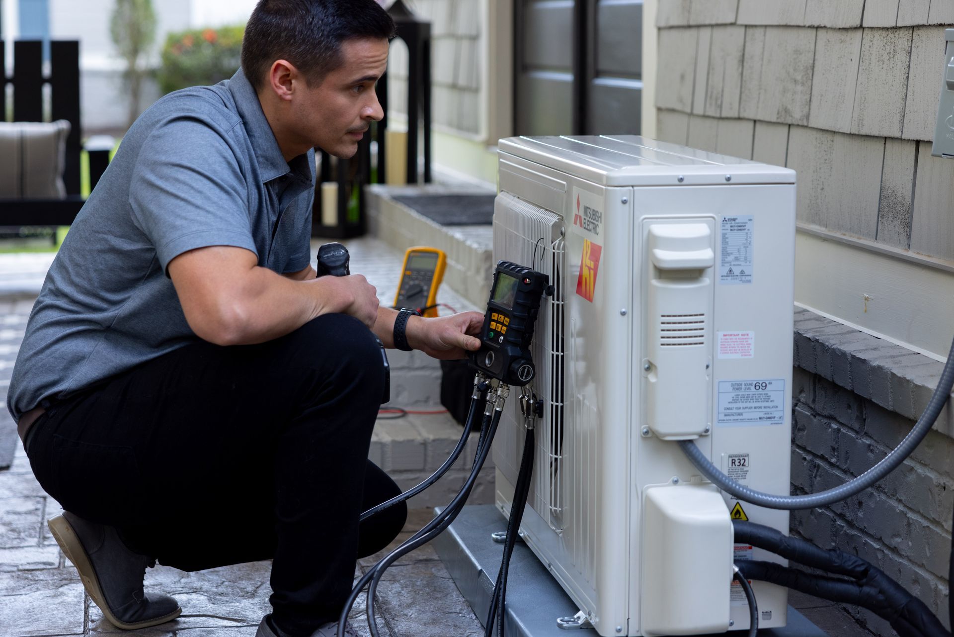 Pfluke Home Services technician checking outdoor AC unit with multimeter. Outdoors on brick.