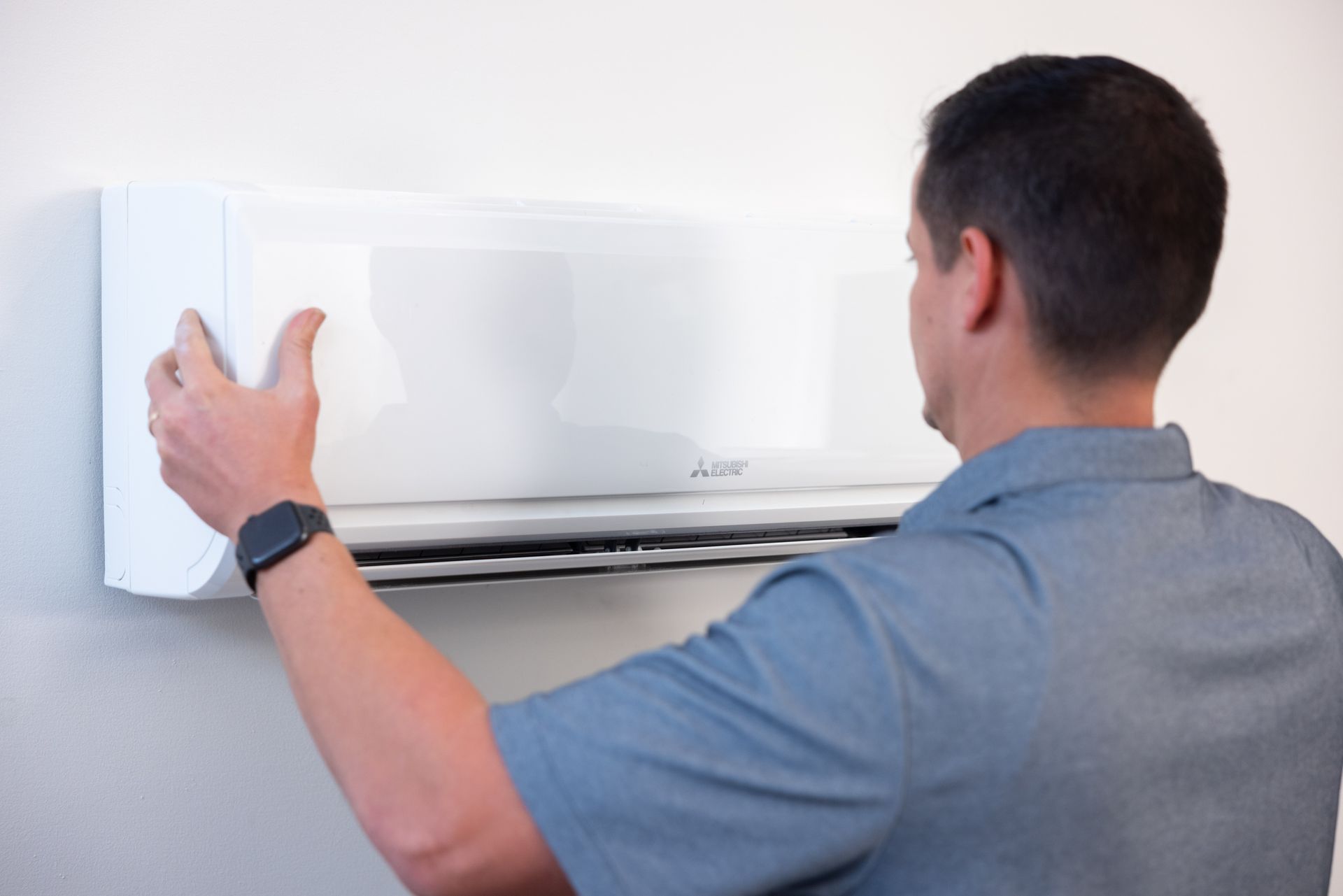 Pfluke Home Services technician installing a white wall-mounted air conditioning unit on a white wall.