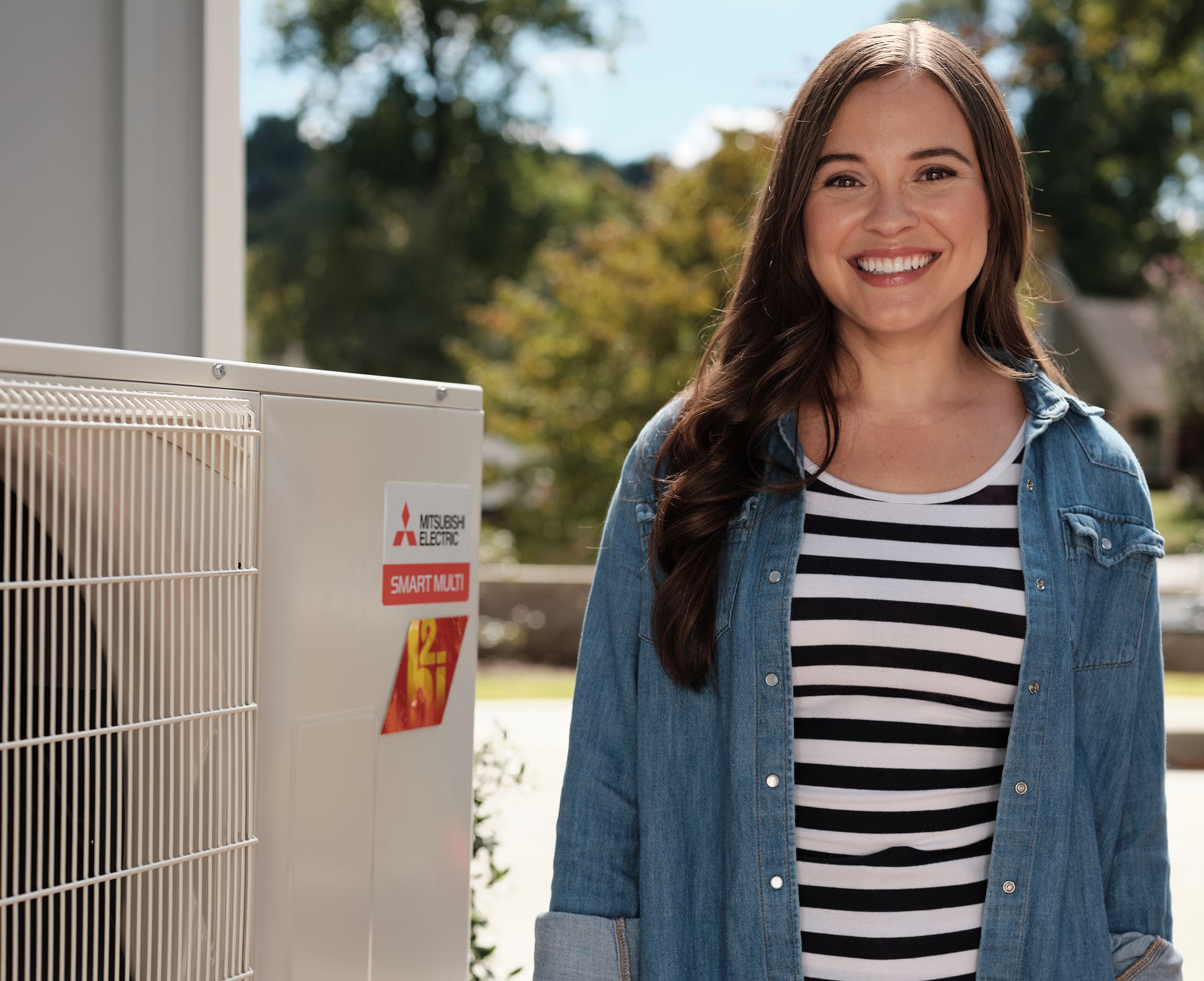 Woman smiles next to a Mitsubishi SmartFlex unit outside a home.