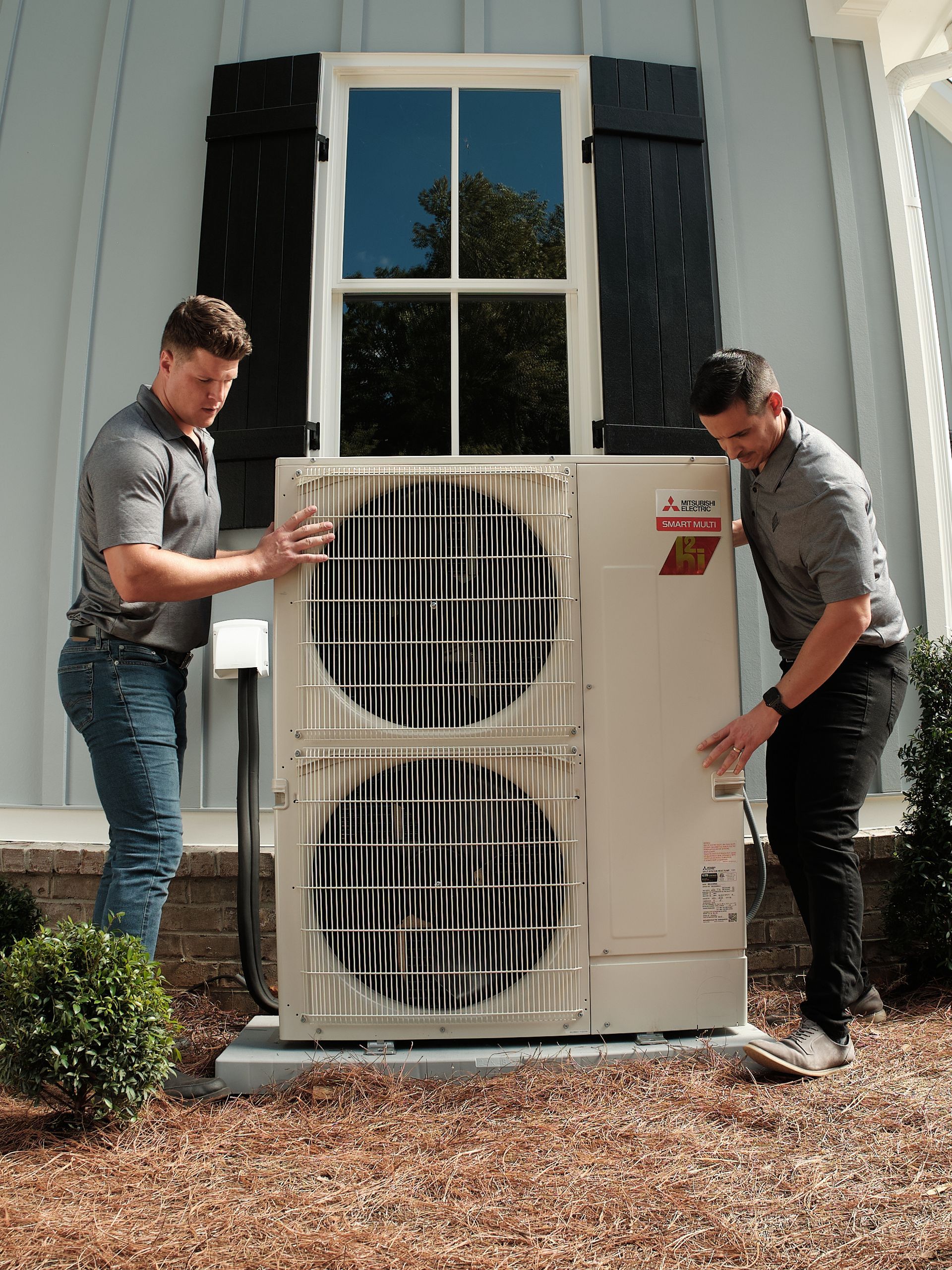 Two Pfluke Home Services technician installing an HVAC unit near a house.