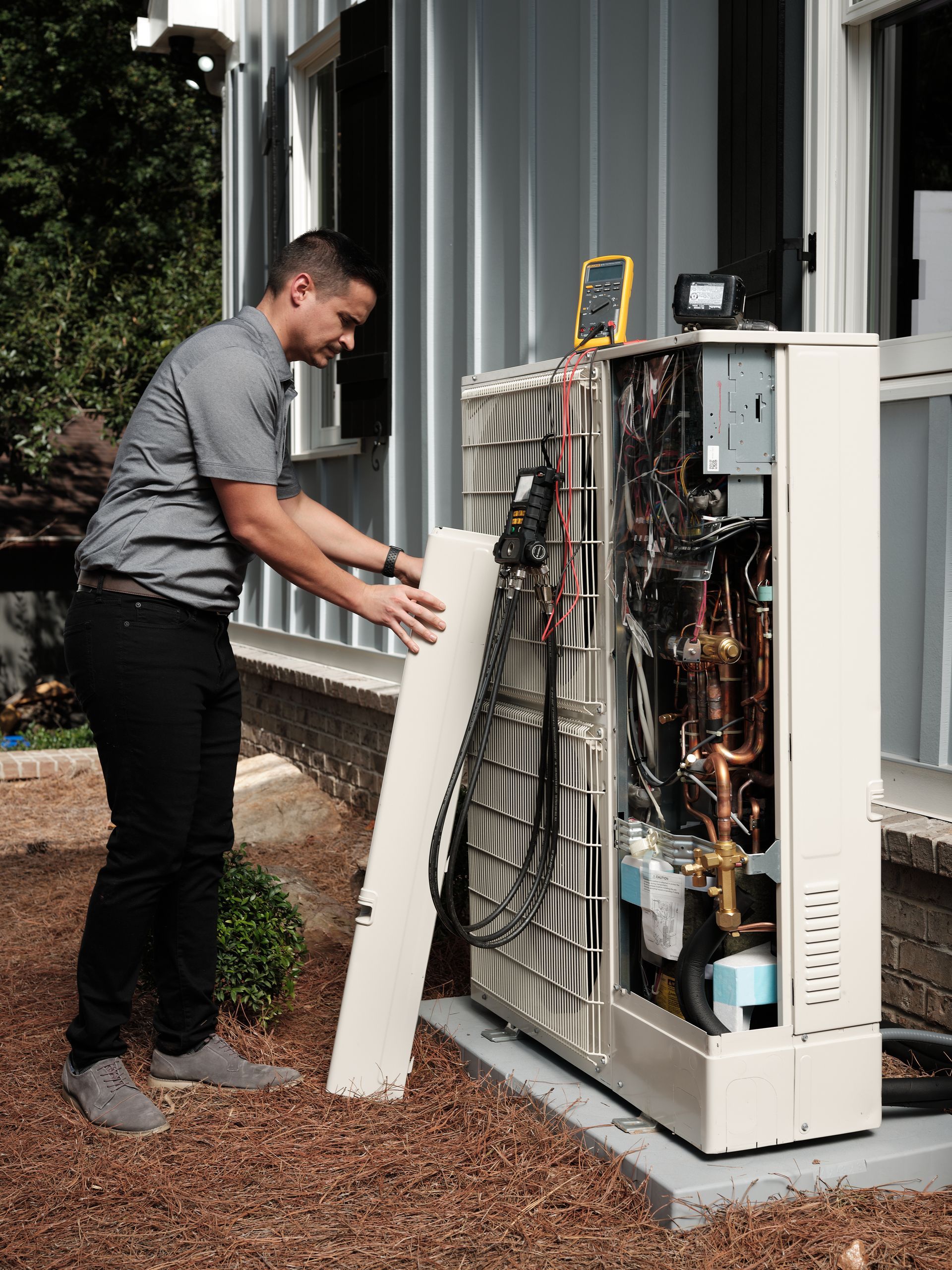 Pfluke Home Services technician inspecting an outdoor HVAC unit, removing a panel.