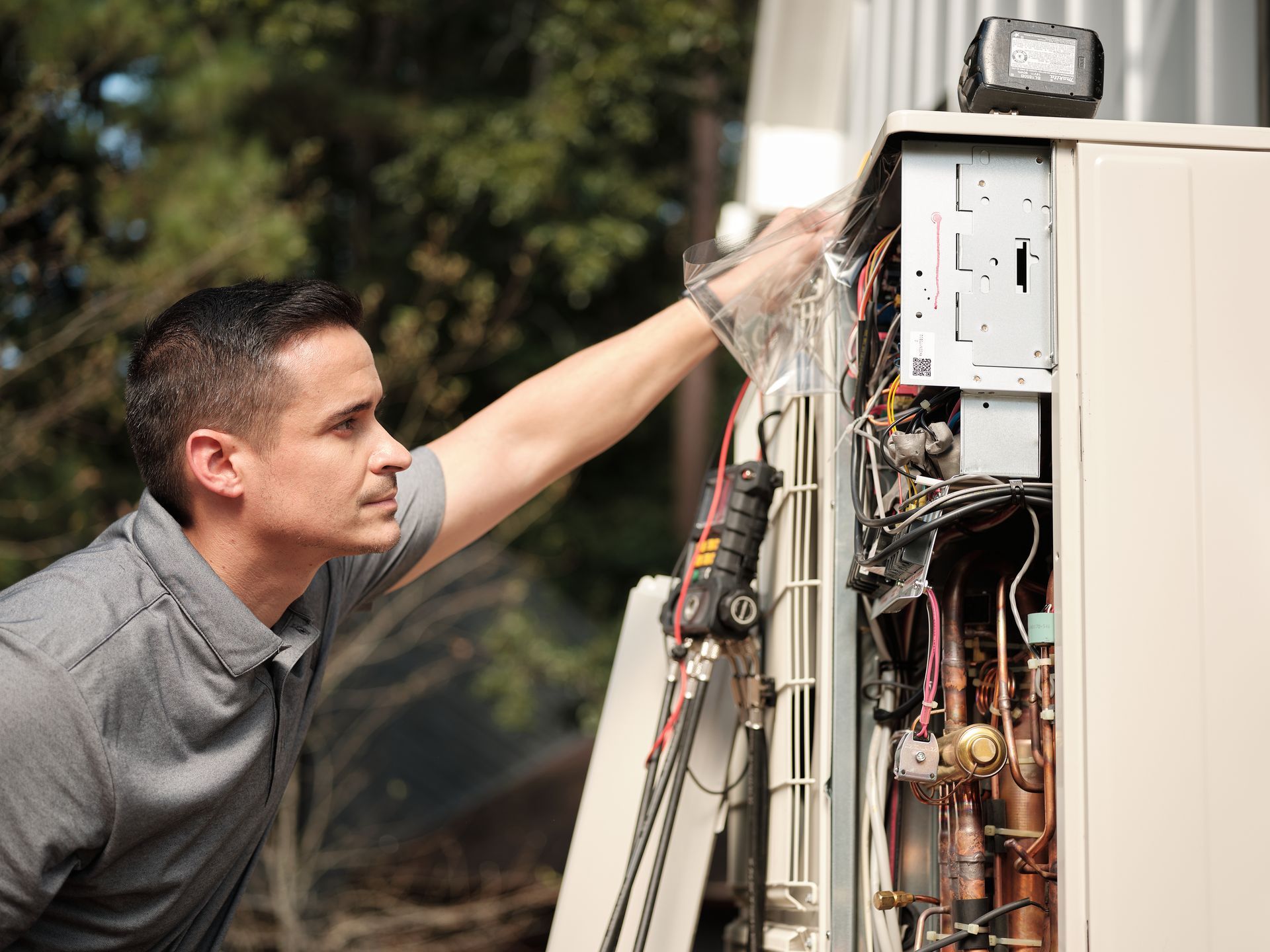 Pfluke Home Services technician inspecting an appliance outdoors, reaching inside to check components.