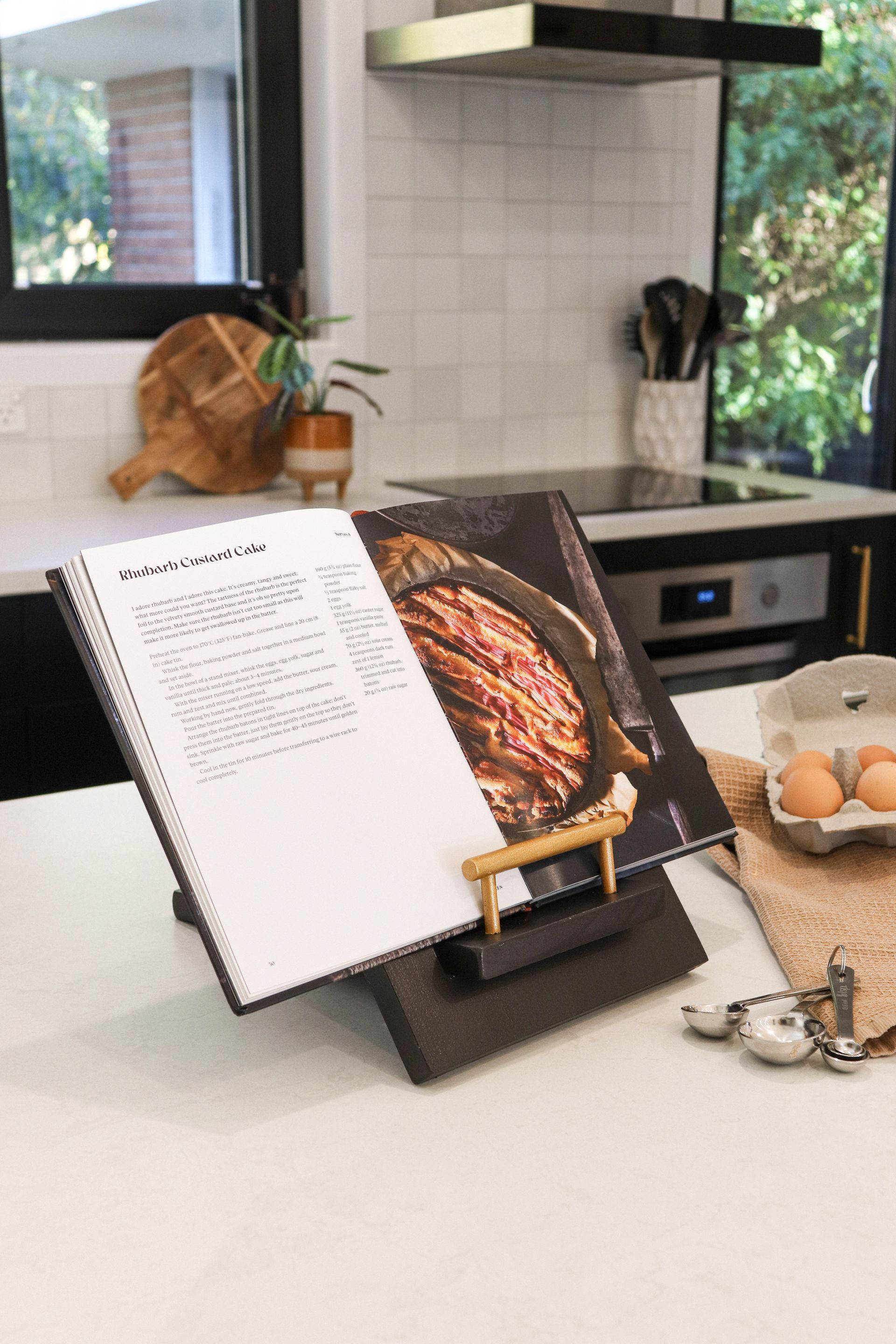 A cookbook is sitting on top of a wooden stand on a kitchen counter.