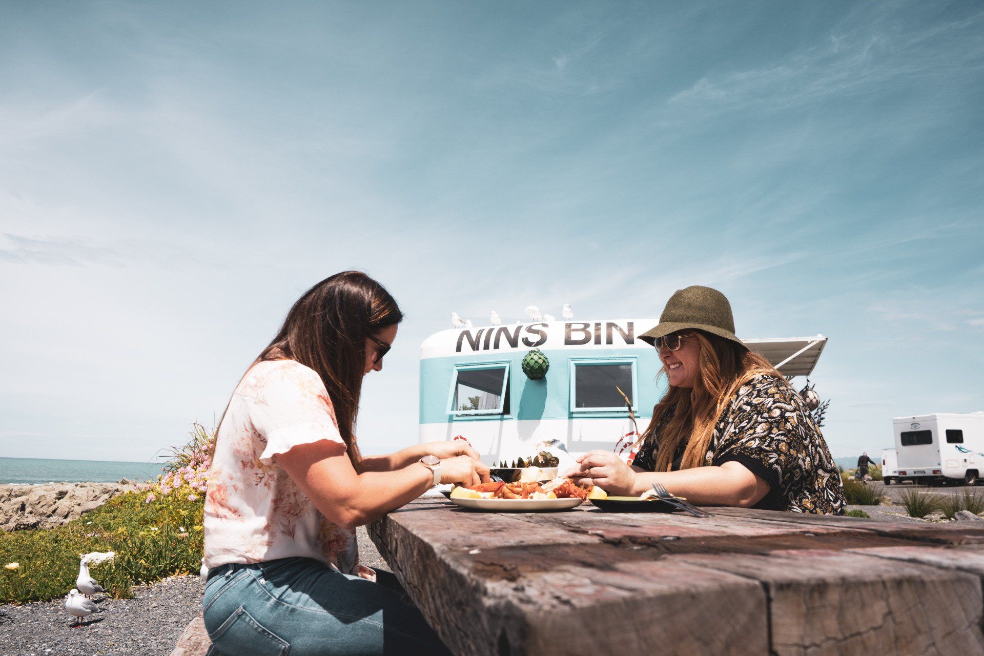 Two women are sitting at a picnic table eating food.