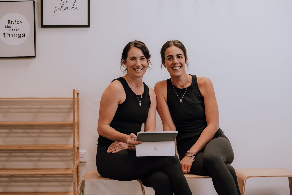 Two women are sitting on a bench looking at a tablet.