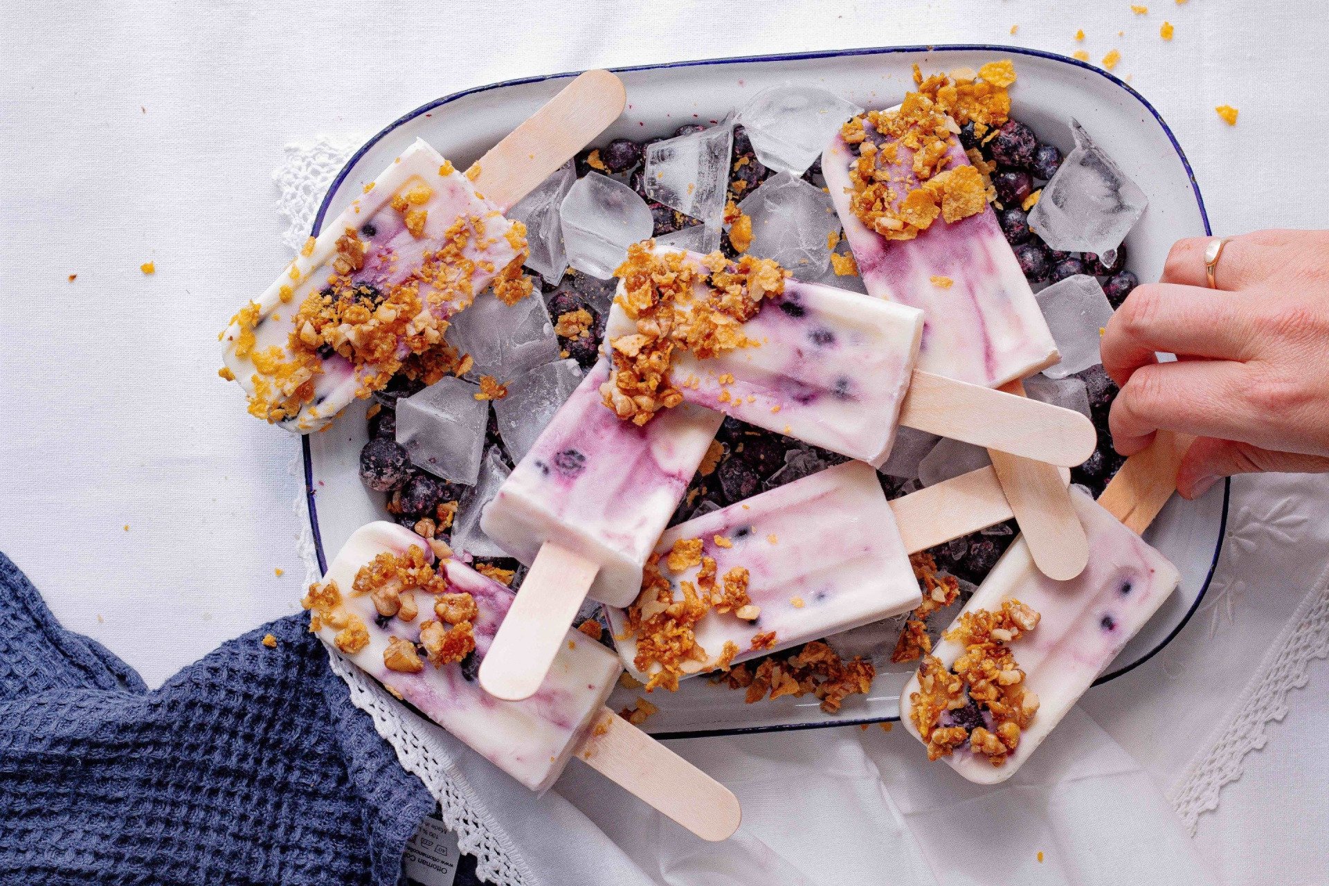 A person is taking a yogurt popsicle from a plate with ice cubes.