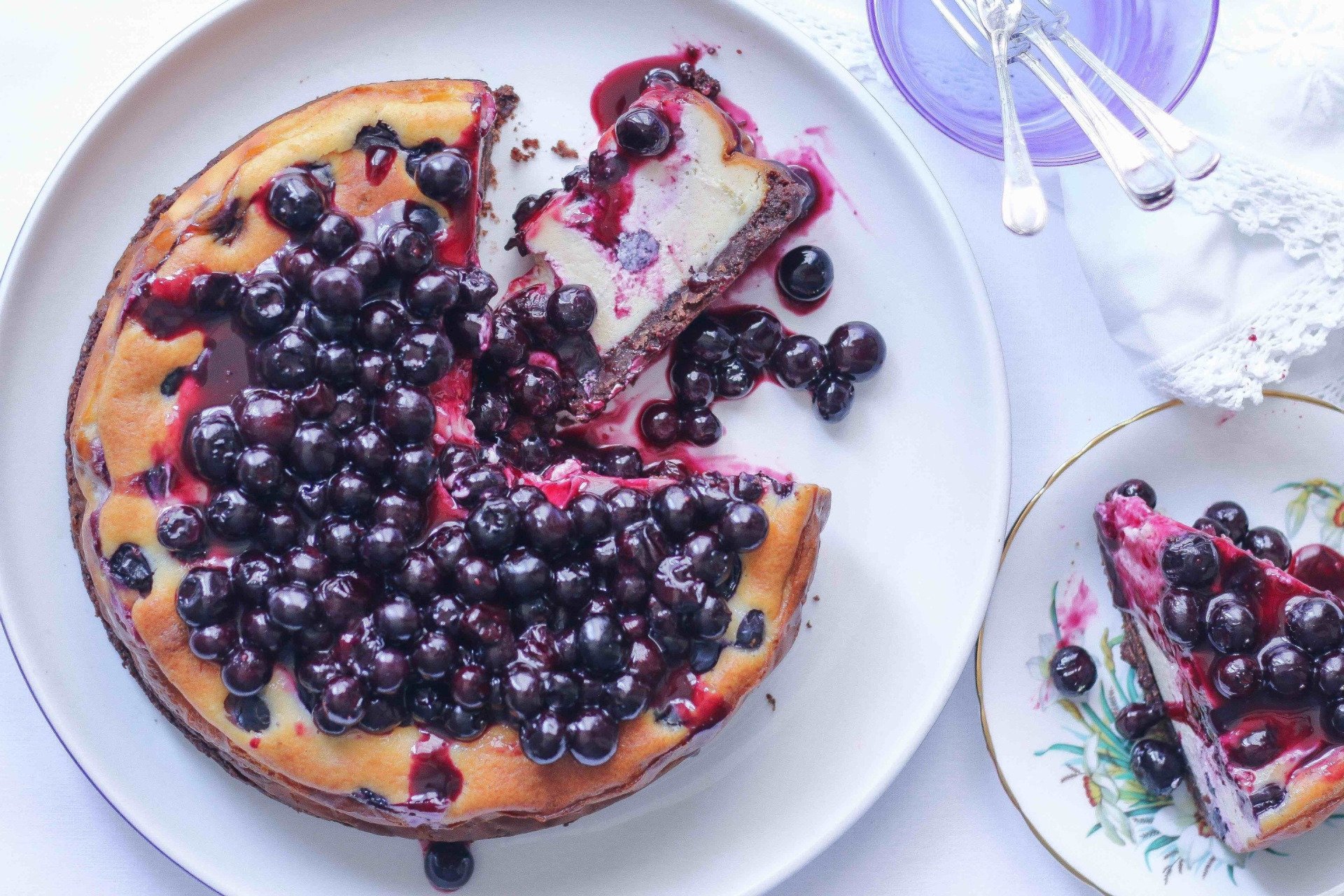 A blueberry cheesecake on a white plate with a slice taken out of it.