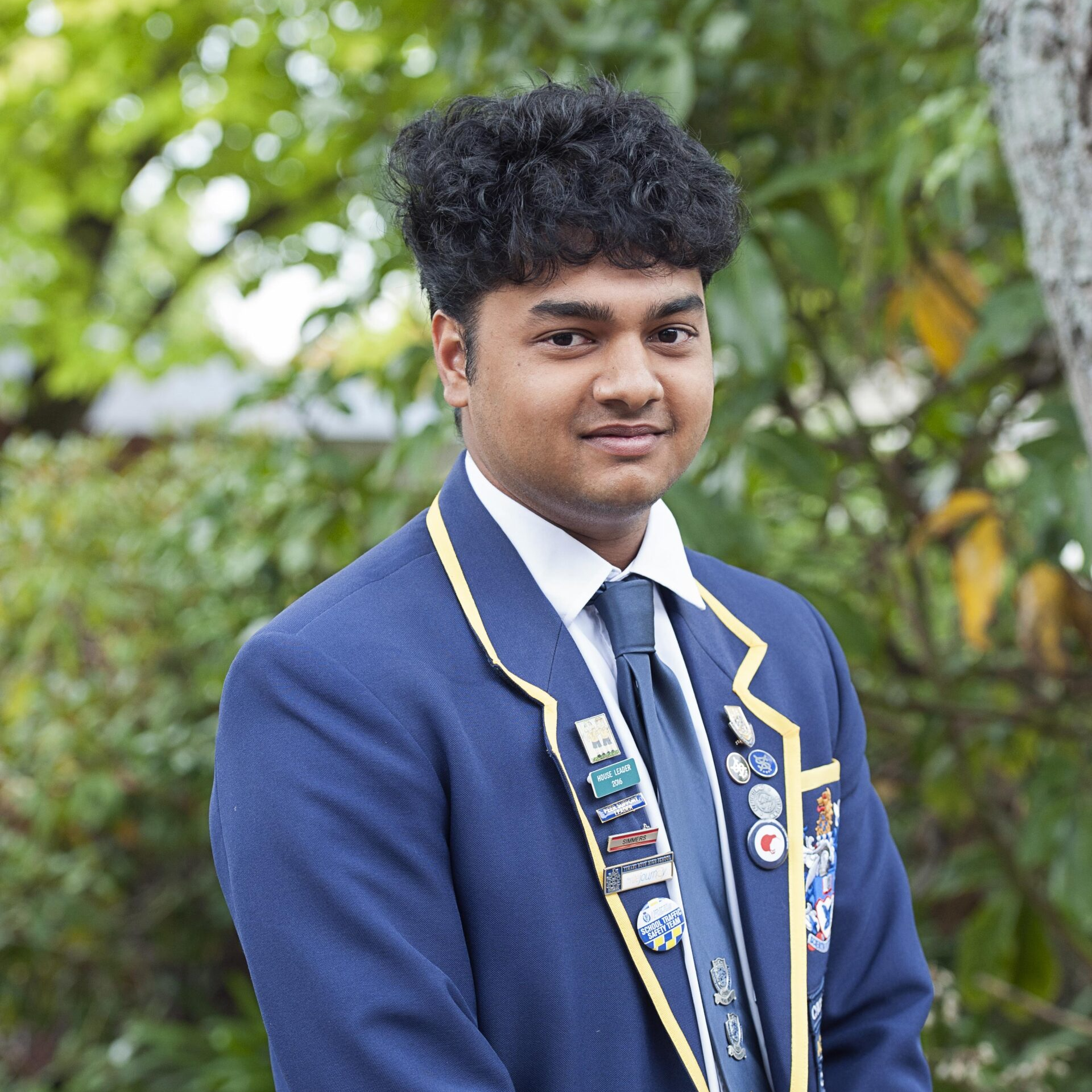 A young man in a blue suit and tie is standing in front of trees