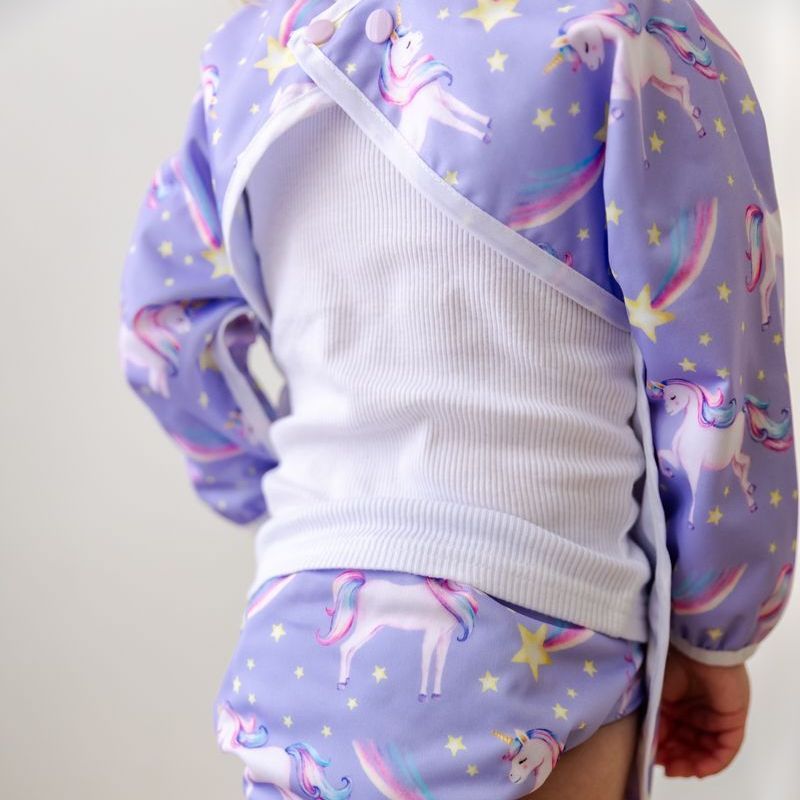 A baby wearing a purple shirt with unicorns on it