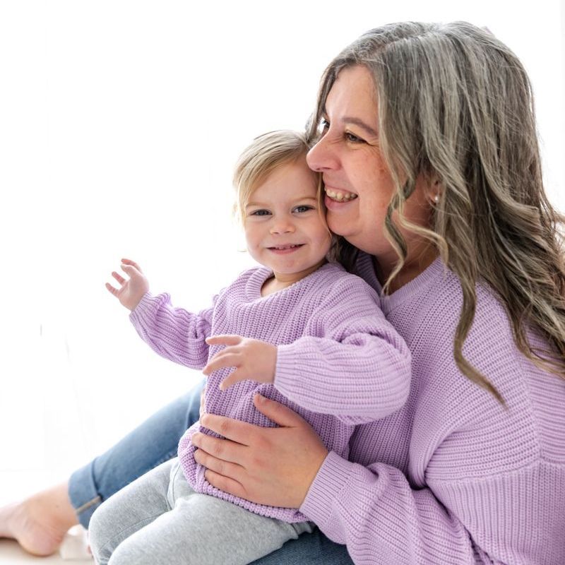 A woman is holding a little girl who is wearing purple sweaters.