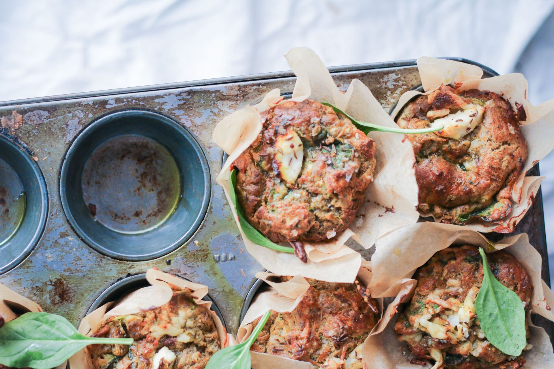 A muffin tin filled with muffins and spinach on a table.