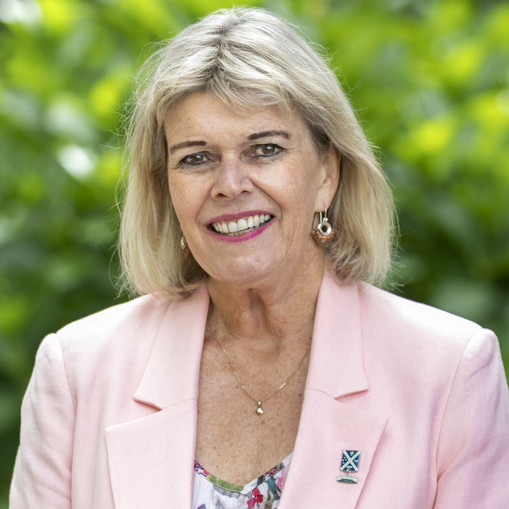 A woman wearing a pink jacket and earrings is smiling for the camera.