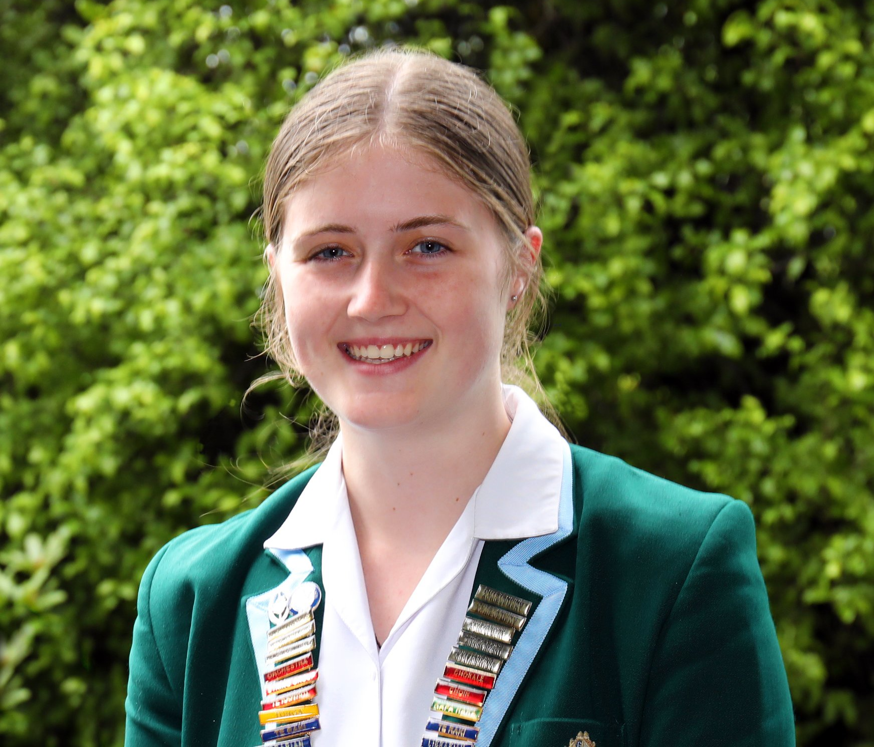 A young woman wearing a green jacket and white shirt smiles for the camera