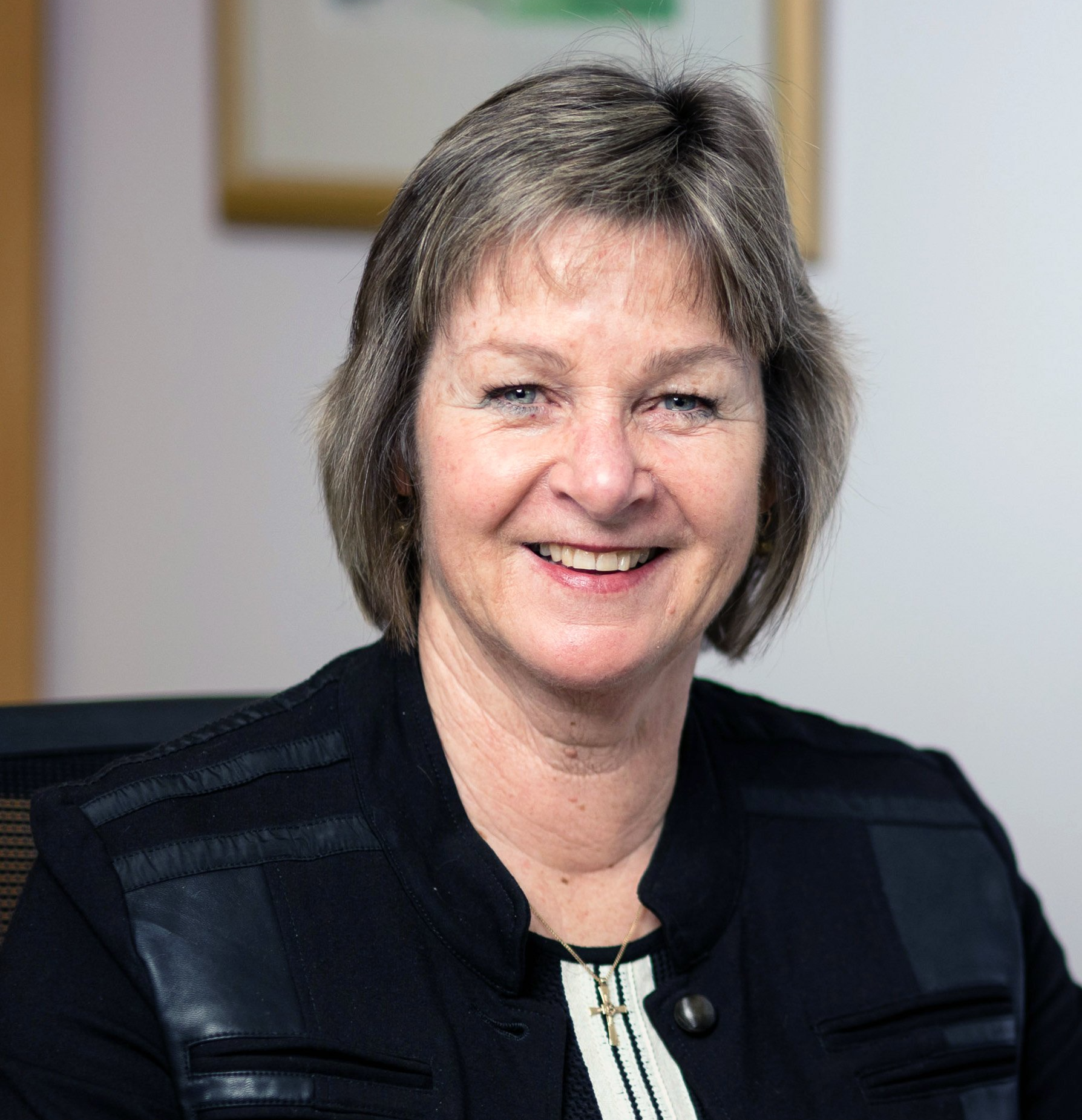 A woman in a black jacket is smiling for the camera while sitting in a chair.