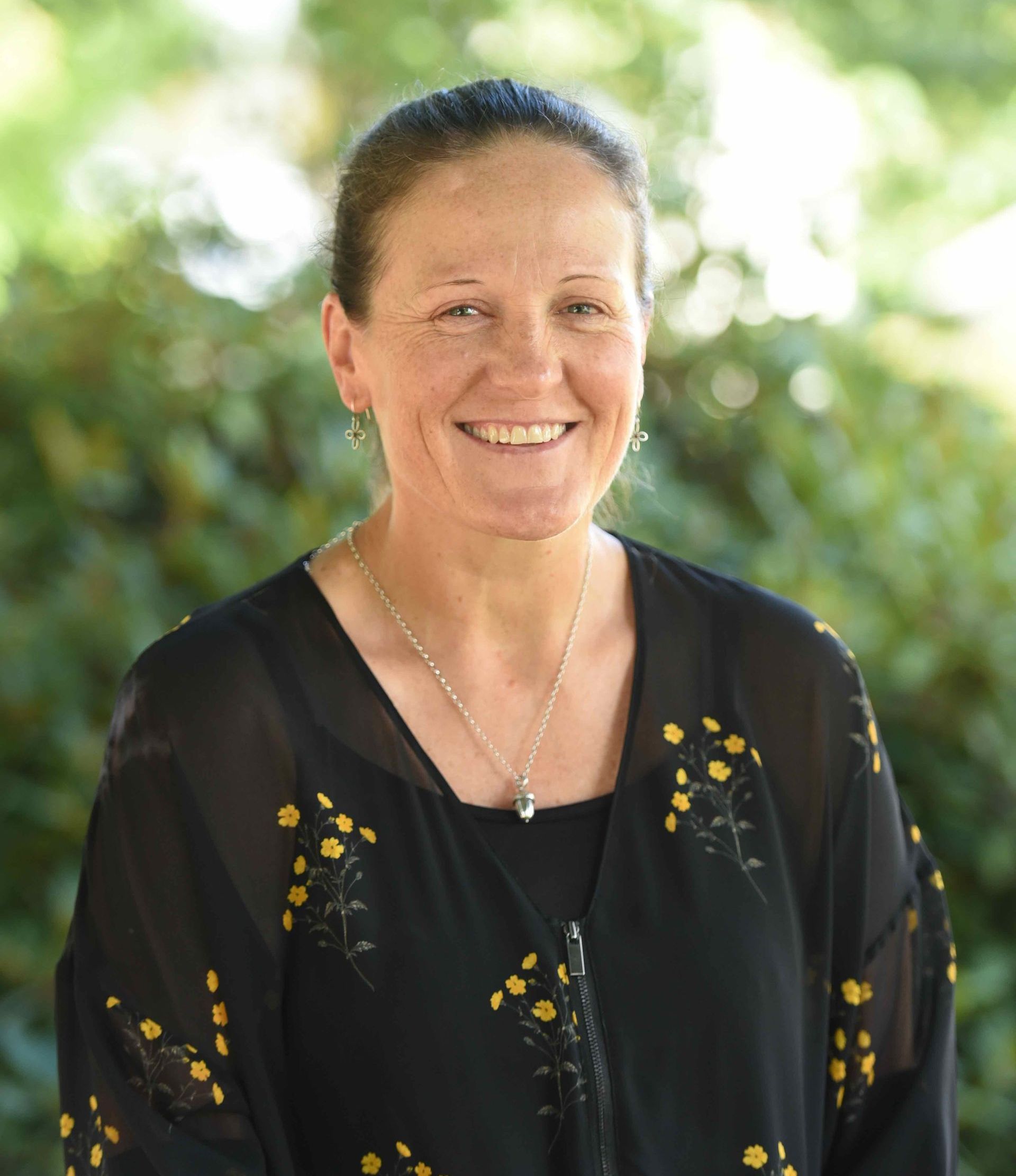 A woman wearing a black shirt and a necklace is smiling for the camera.