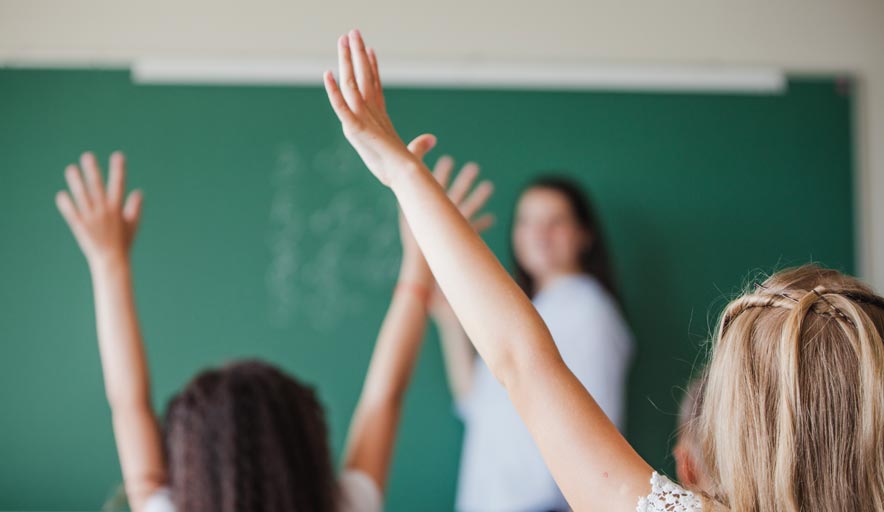 A group of students are raising their hands in a classroom to answer a question.