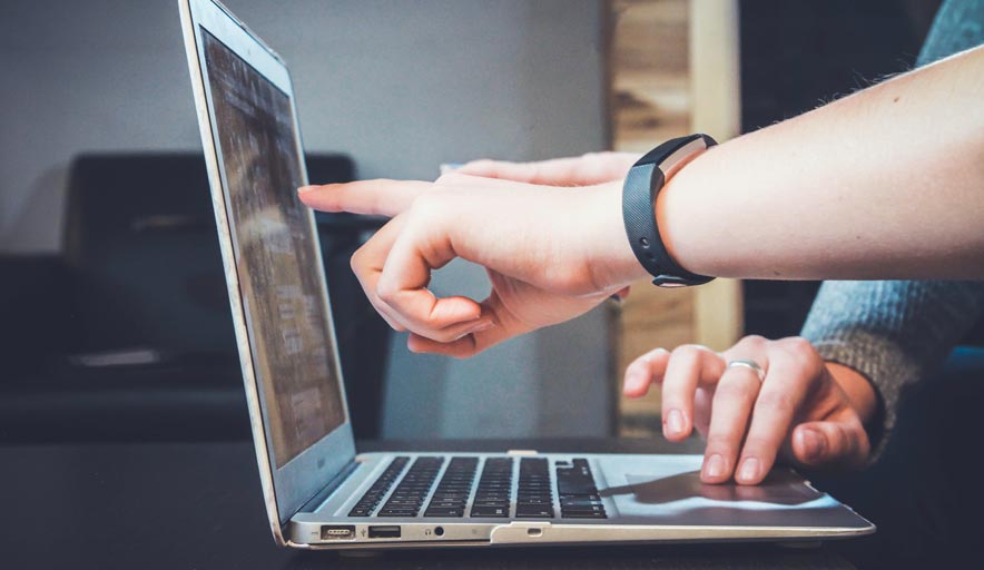 A person is using a laptop computer and pointing at the screen.