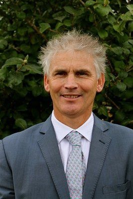 A man in a suit and tie is standing in front of a bush.