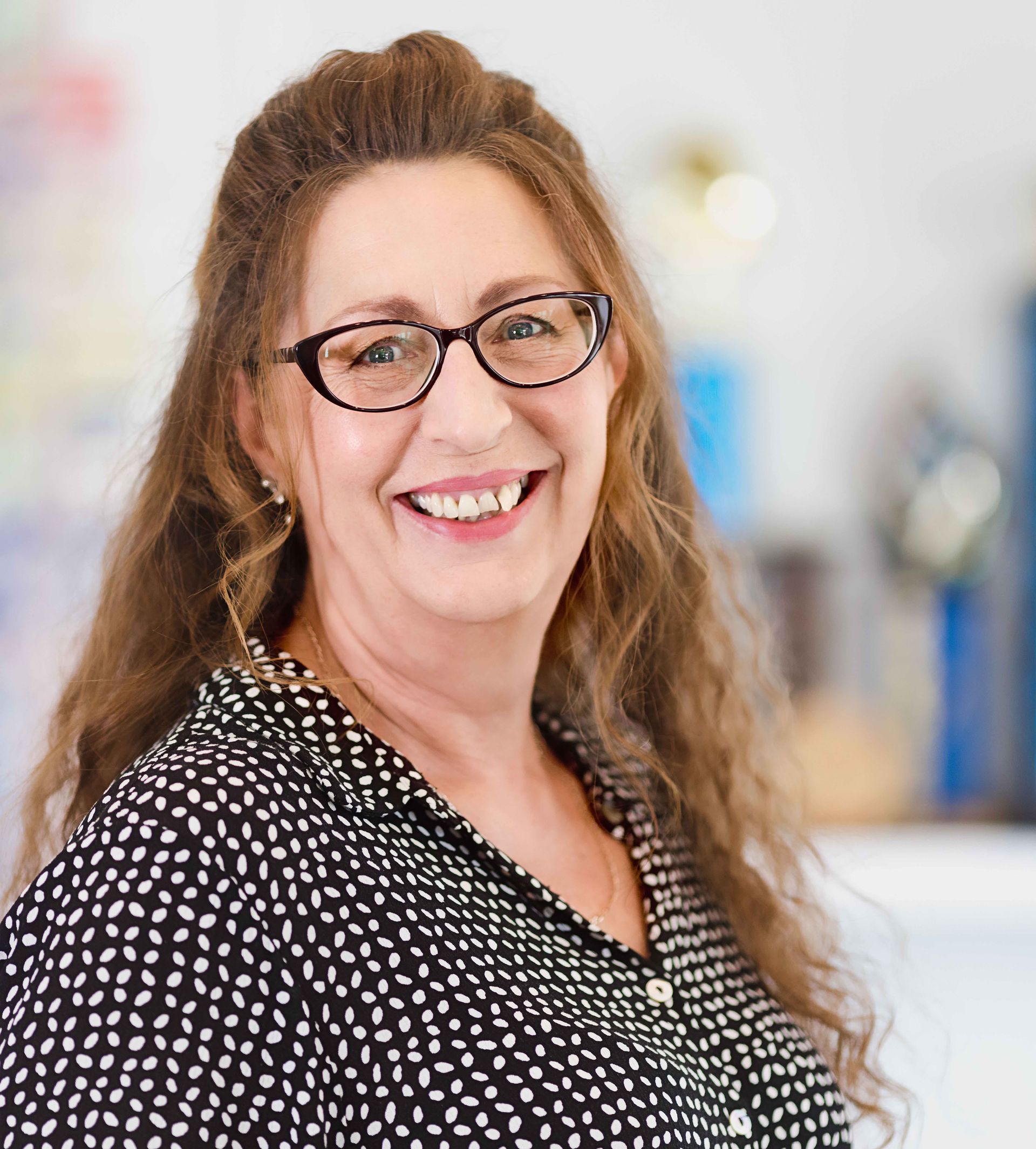 A woman wearing glasses and a black and white polka dot shirt is smiling for the camera.