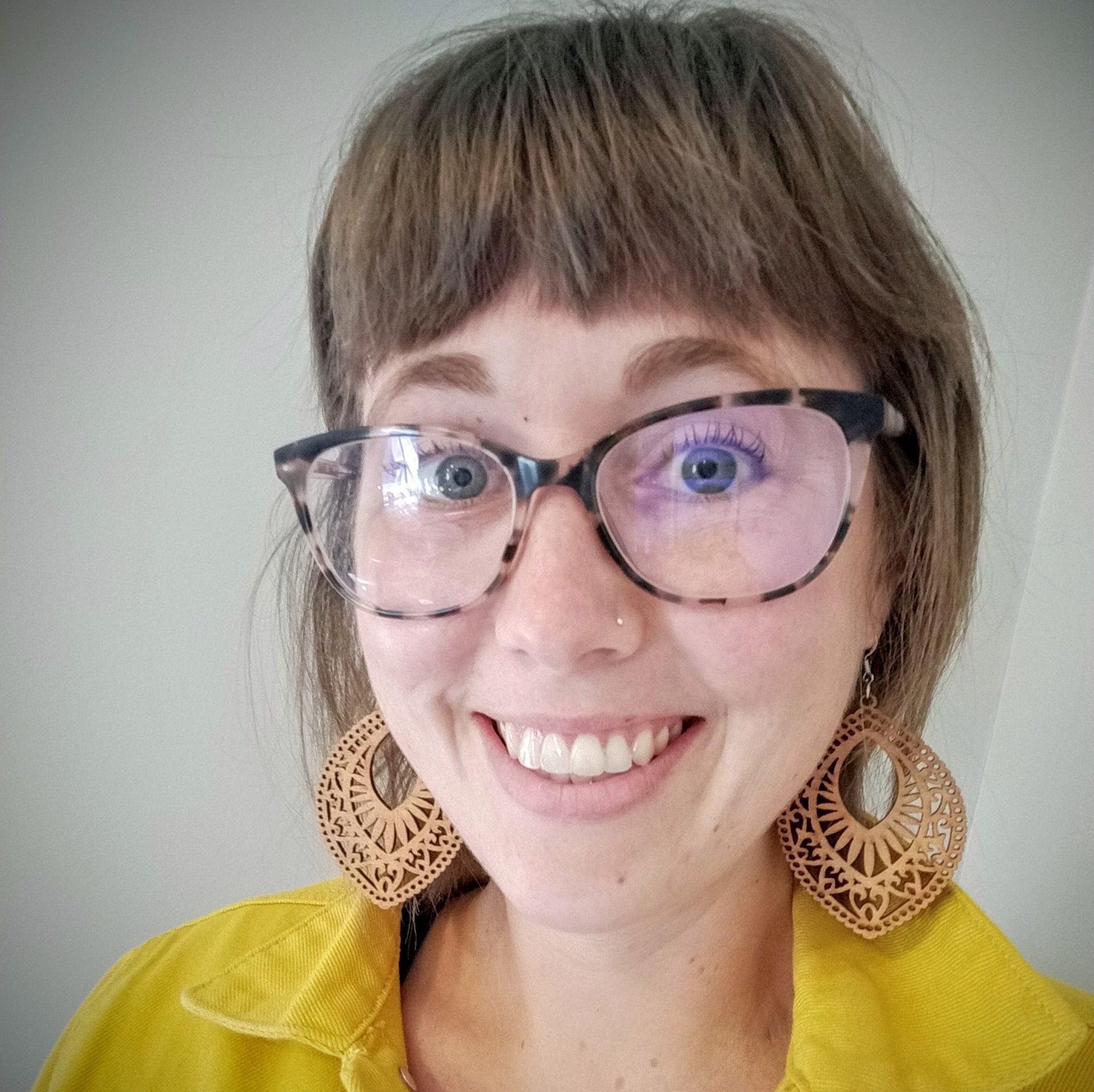 A woman wearing glasses and earrings is smiling for the camera.