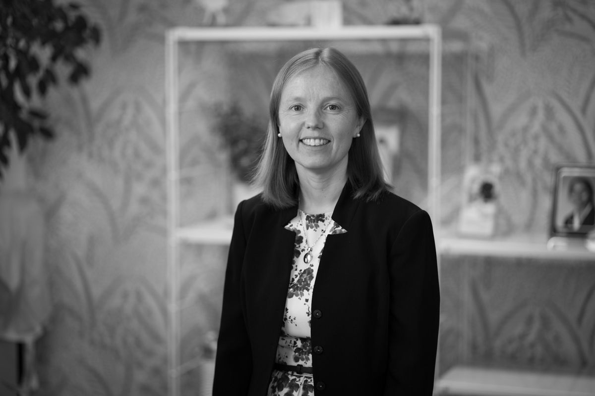 A black and white photo of a woman in a suit standing in front of a bookshelf.