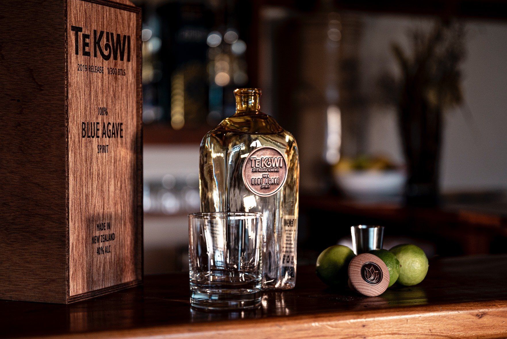 A bottle of tequila is sitting on a wooden bar next to a glass.