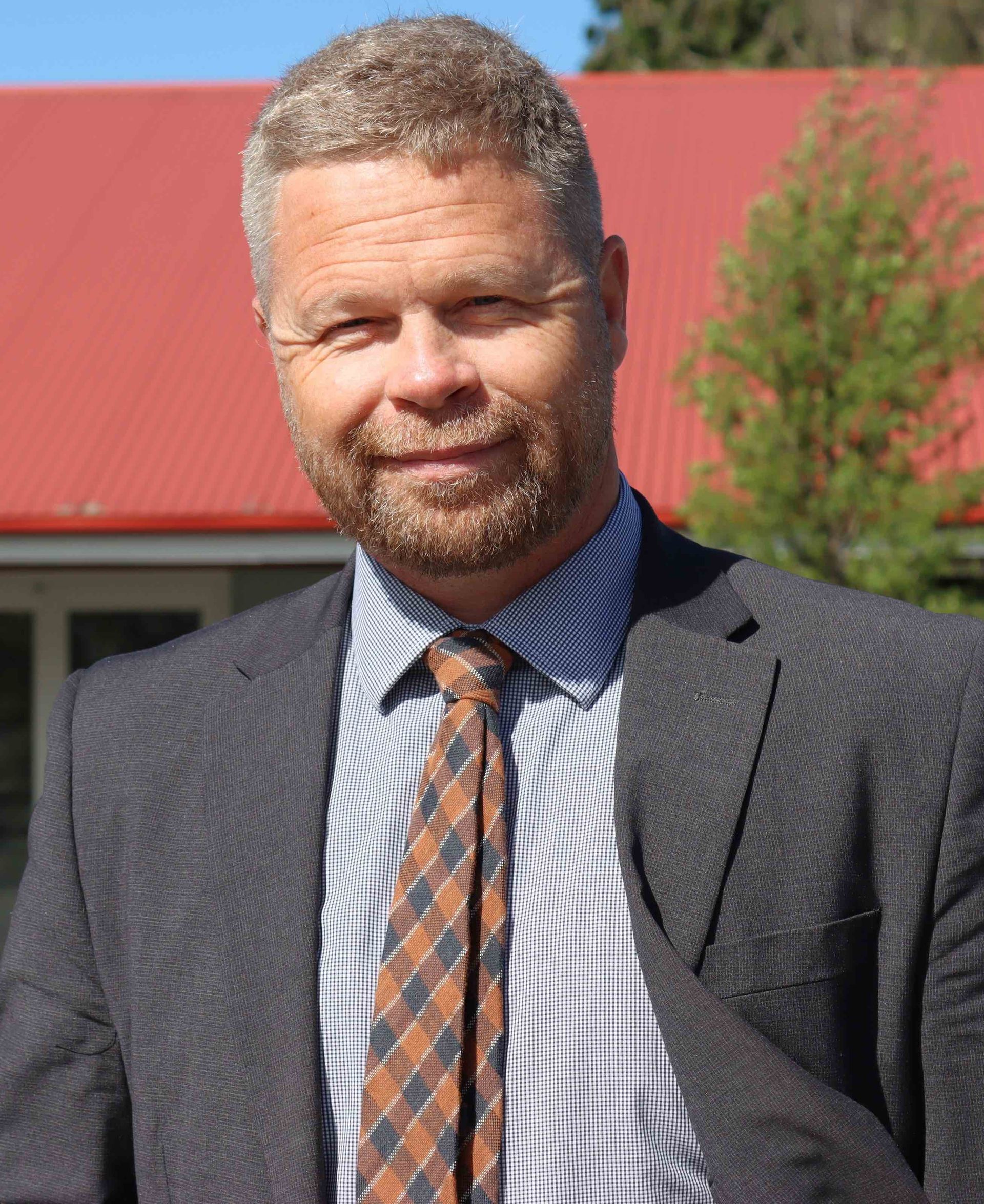 A man in a suit and tie is standing in front of a red roof.