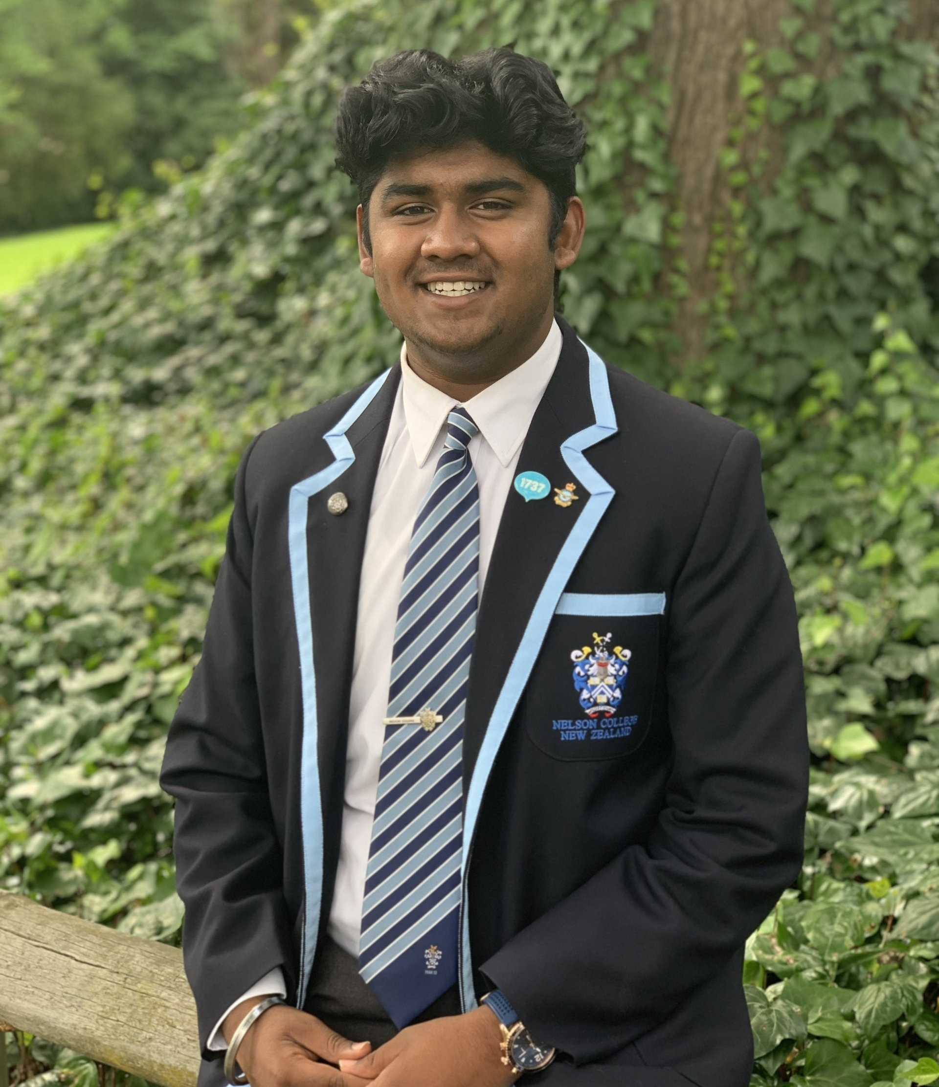 A young man in a suit and tie is standing in front of a bush.