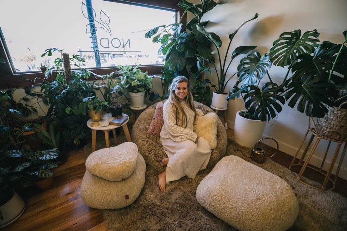 A woman is sitting in a bean bag chair in a living room surrounded by plants.